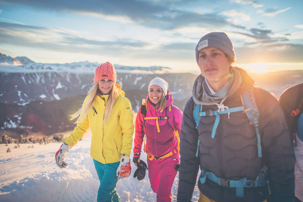 Group of young hikers enjoying a winter hike on the Plose with sunset light and Alpine mountain views.
