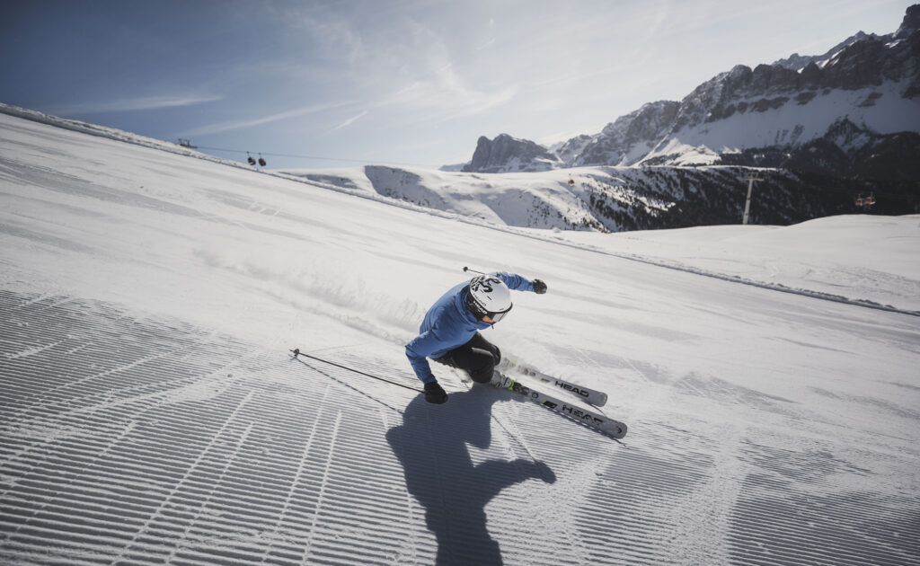 Skier carving on a freshly groomed slope on the Plose with panoramic views of the snowy Dolomites.
