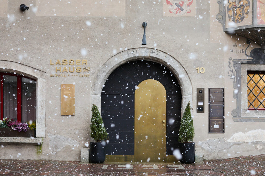 Entrance of the Arthotel Lasserhaus in Brixen during winter snowfall, featuring a golden door and historic facade.